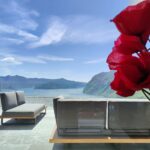 Bright red flowers in foreground with panoramic view of Lake Iseo from a serene terrace