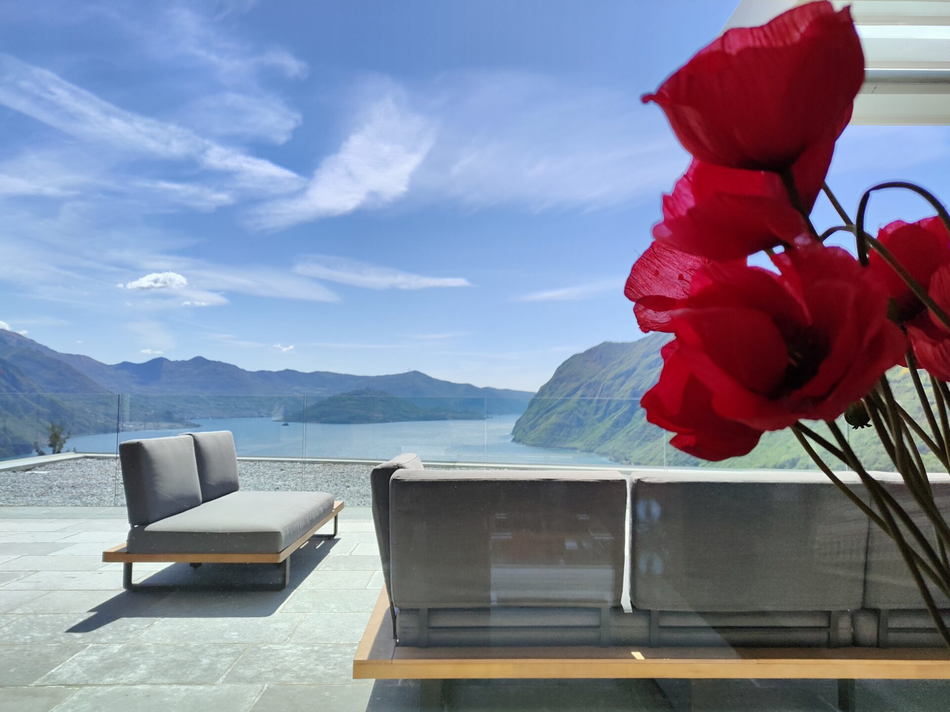 Bright red flowers in foreground with panoramic view of Lake Iseo from a serene terrace