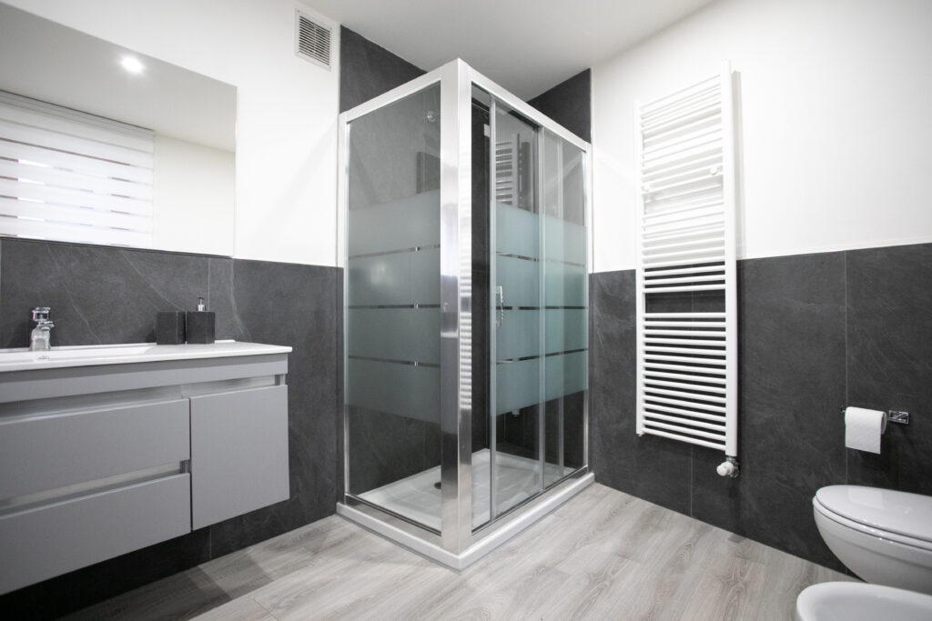 Sleek modern bathroom with glass shower enclosure and dark grey tiles in Lovere apartment