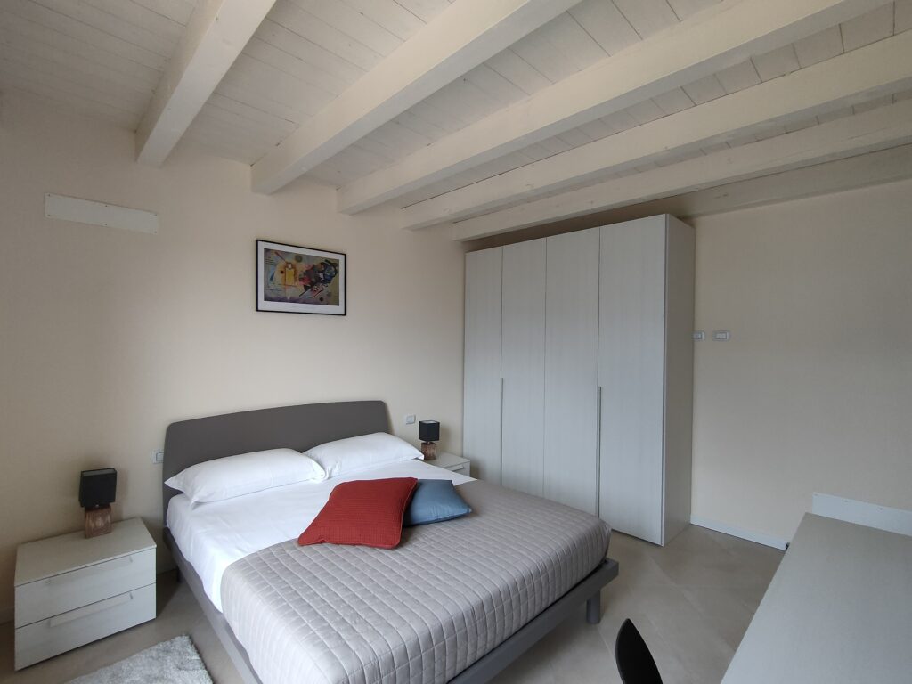 A modern and serene bedroom with exposed wooden beams in Casa Cuneo by Fabula Home Rental