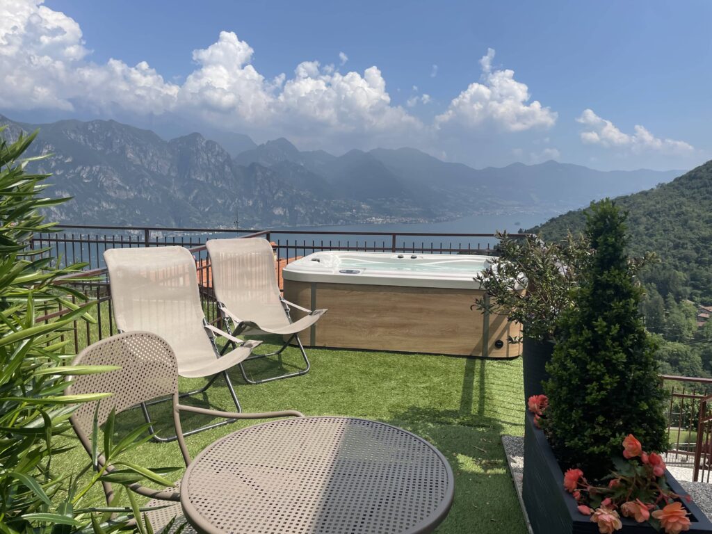 Casa il Nido's terrace with a hot tub, seating area, and vibrant flora, overlooking Lake Iseo, by Fabula Home Rental