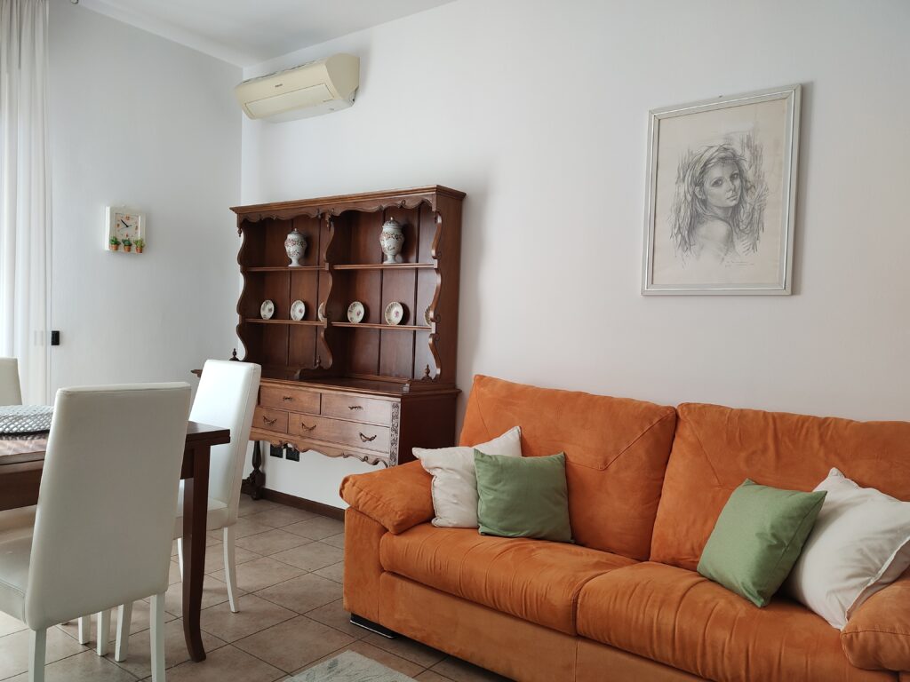 Intimate corner in GiannaRosa Apartment featuring an orange sofa, wooden shelving, and a captivating pencil artwork, located in Lovere