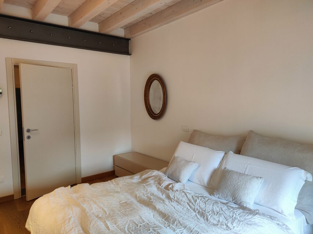 Cozy and minimalistic bedroom design with plush bedding and a rustic wooden beam ceiling at Lakeview Apartment