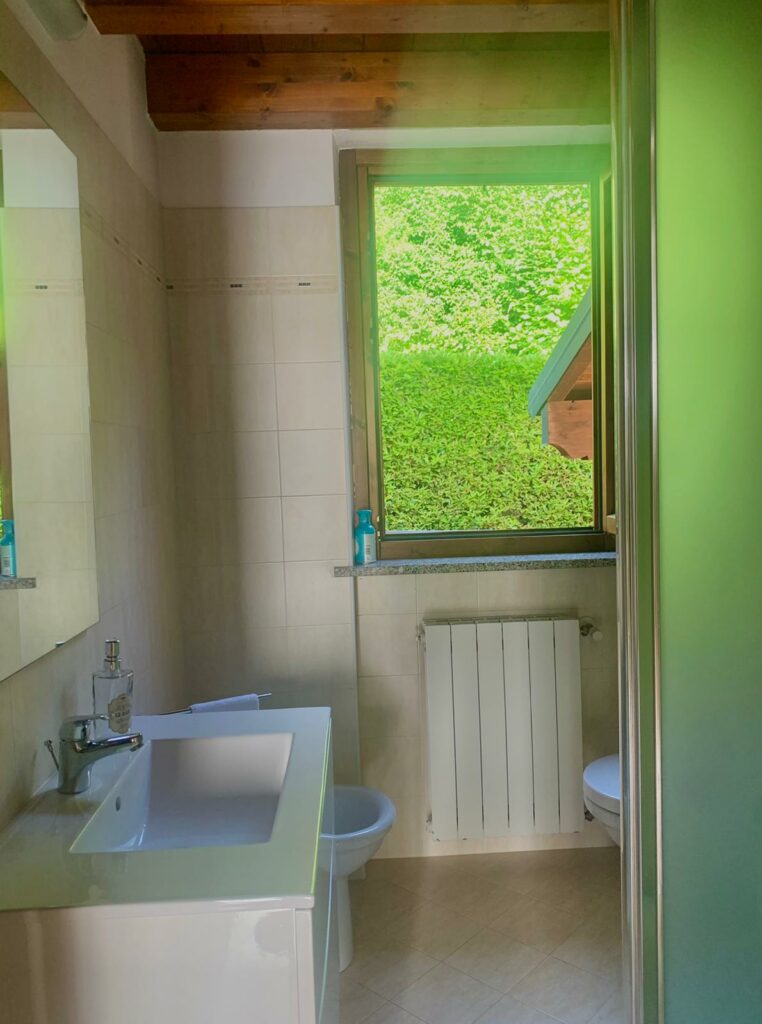 Bright and serene bathroom with a view of lush greenery outside the window in La Rocca apartment