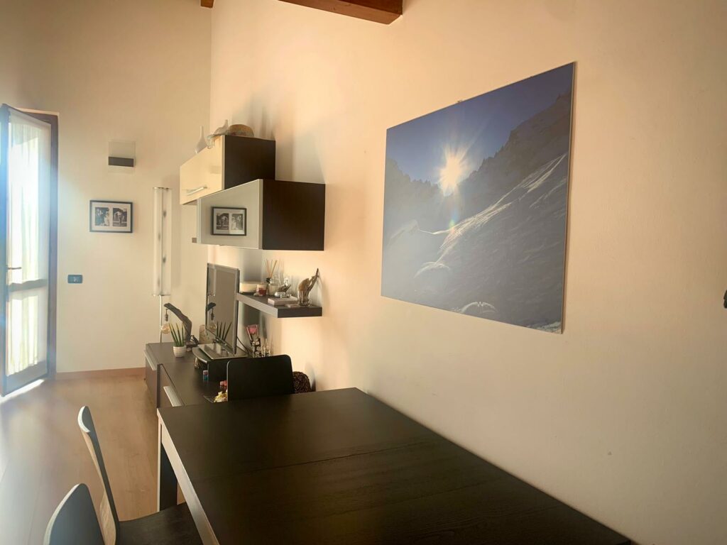 Cozy dining area in La Rocca apartment, illuminated by natural sunlight with a striking mountain canvas on the wall