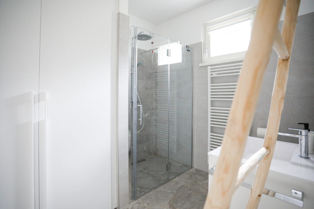 Modern glass-enclosed shower area with gray tiles at Seliera