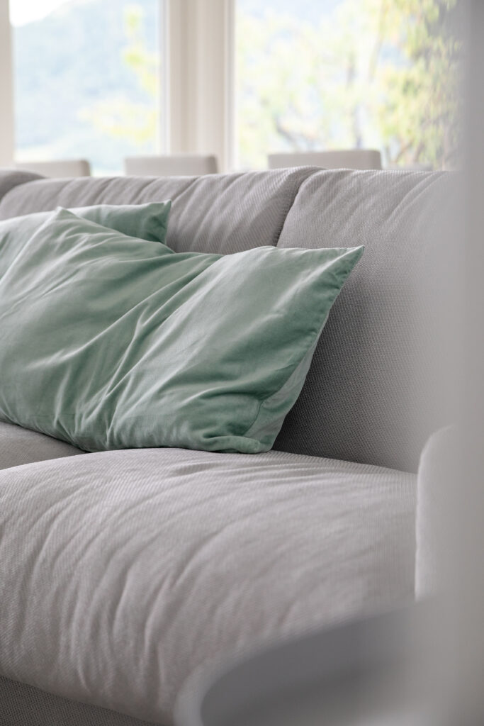 A close-up of plush cushions on a textured sofa at Trivia Resort, with a glimpse of Lake Iseo in the distance