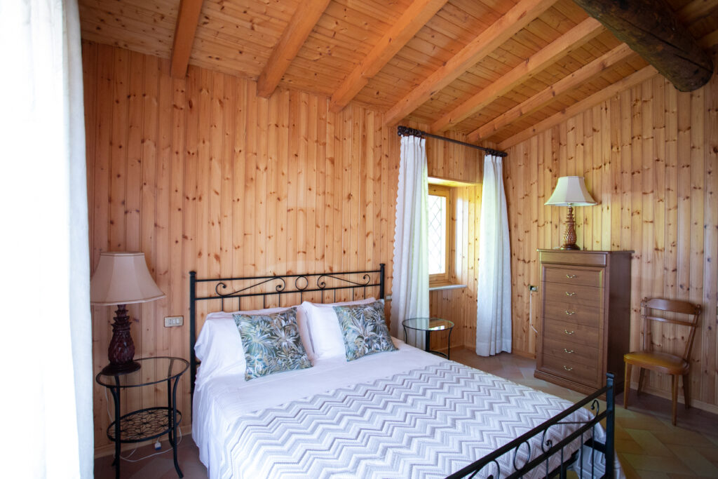 Cozy master bedroom with wrought iron bed, wooden paneling, and warm natural light in Villa Simone